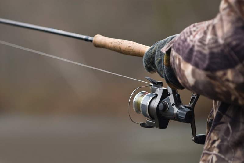 A gloved hand holds fishing rod and reel in a Michigan winter.